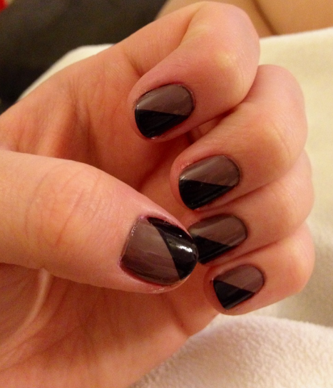 Short, rounded nails with a glossy taupe base and diagonal black color blocking, offering a striking geometric idea for nail designs for short nail beds.