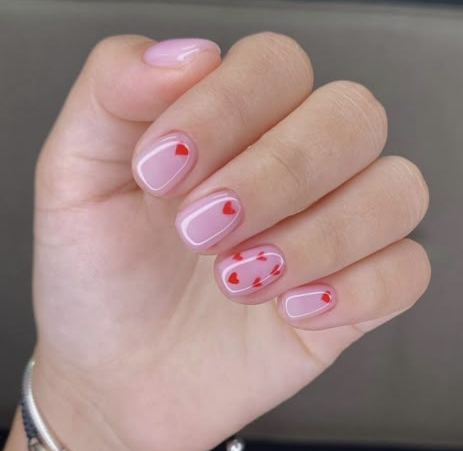 Short, rounded nails with a glossy translucent pink base decorated with cute red heart accents, offering a sweet option for nail designs for short nail beds.