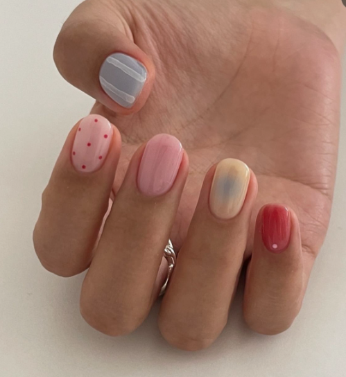 Short, rounded nails featuring an eclectic mix of pastel colors, polka dots, stripes, and an aura effect, providing a playful and creative style for nail designs for short nail beds.
