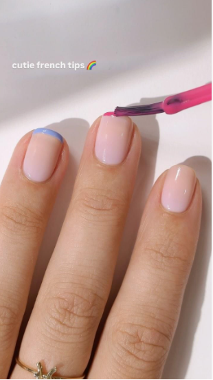 Short, squared-off nails featuring a glossy neutral base and vibrant pastel-colored french tips being painted, offering a fun inspiration for nail designs for short nail beds.