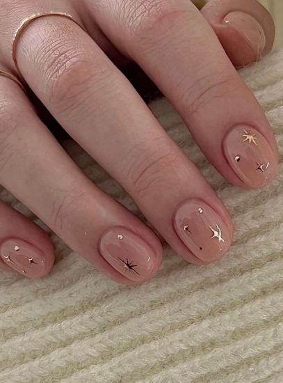 Short, rounded nails with a glossy nude base decorated with delicate metallic star and dot charms, making it a celestial option for nail designs for short nail beds.