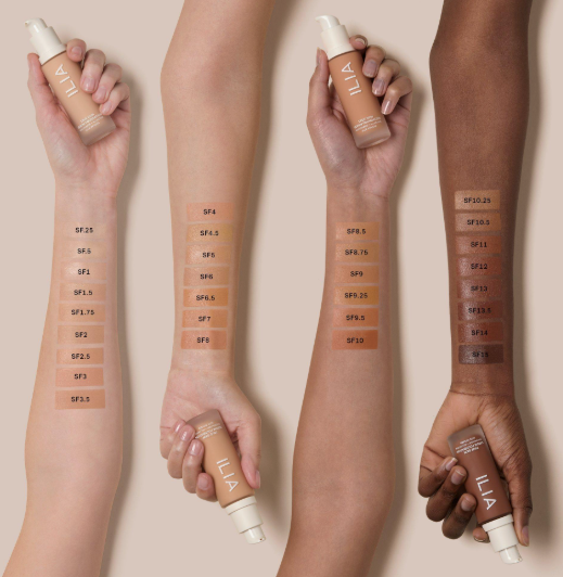 A beauty product shot showcasing Spring 2026 makeup trends, featuring four arms displaying various Ilia foundation shade swatches ranging from fair to deep tones.