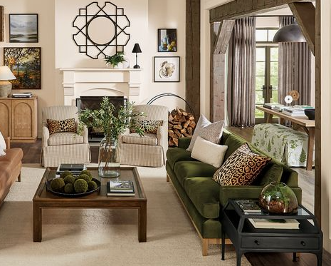 A warm, eclectic living room featuring an olive green velvet sofa, patterned armchairs around a fireplace, a dark wooden coffee table, and rich decor accents, beautifully demonstrating how to decorate when everything doesn't match.