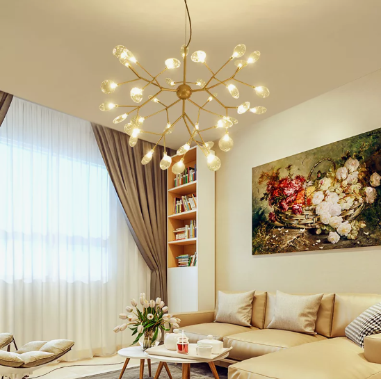 A brightly lit living room showcasing a branching gold chandelier, neutral seating, a tall built-in bookshelf, and a large floral painting, demonstrating a stylish approach to how to decorate when everything doesn't match.