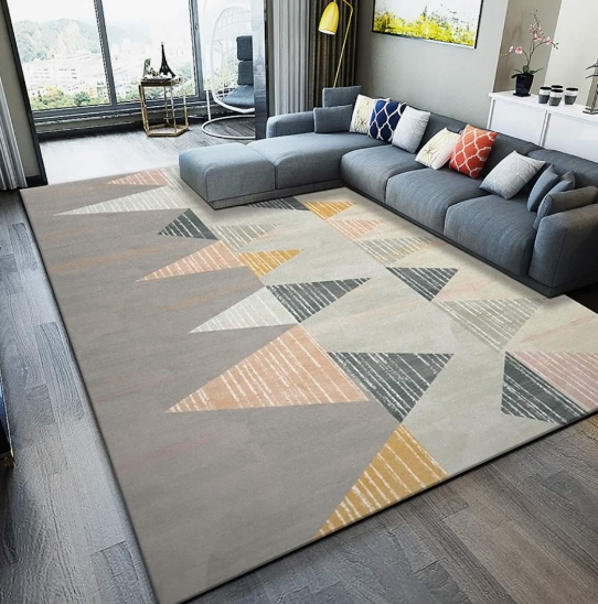 A modern living room featuring a gray sectional sofa with multicolored accent pillows and a large area rug with abstract geometric triangles, showcasing how to decorate when everything doesn't match.