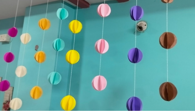Several vertical strands of hanging 3D paper globe garlands in various colors including pink, yellow, blue, purple, and brown, illustrating cheap DIY crafts on a budget.