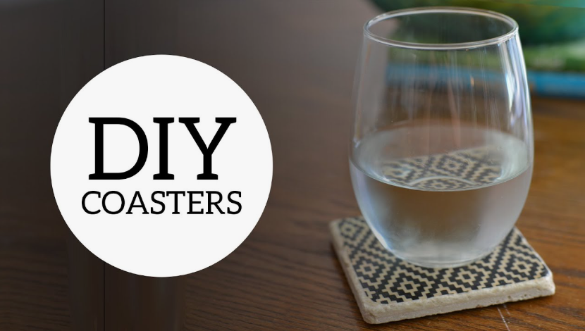 A square ceramic tile coaster featuring a black and white geometric pattern, with a glass of water resting on top of it on a wooden surface, showcasing cheap DIY crafts on a budget.
