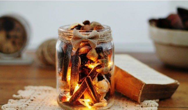 A glass mason jar filled with potpourri and warm fairy lights, wrapped around the neck with twine and a burlap bow, showcasing cheap DIY crafts on a budget.