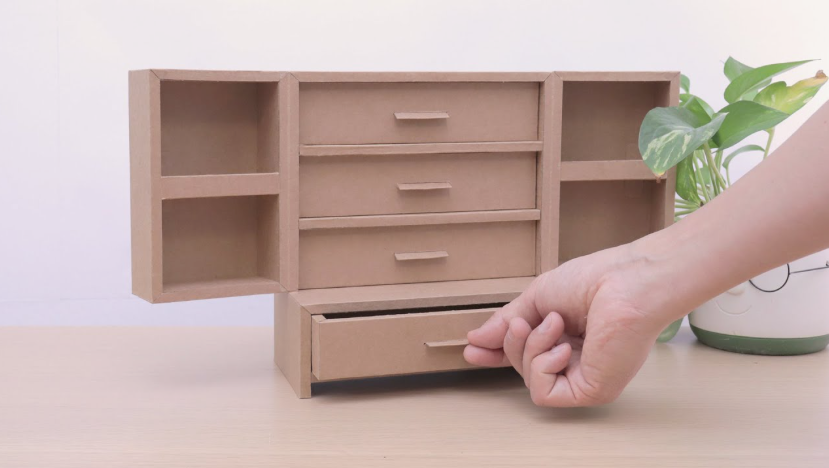 A handmade miniature desk organizer constructed from brown cardboard with open cubbies and several small sliding drawers, showcasing cheap DIY crafts on a budget.