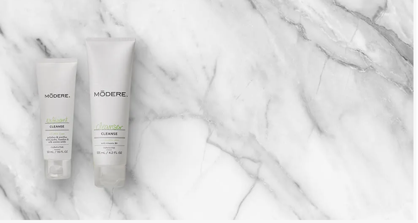 Two Modere skincare tubes of exfoliant and cleanser arranged on a white marble background, showcasing beauty tips for women over 40.