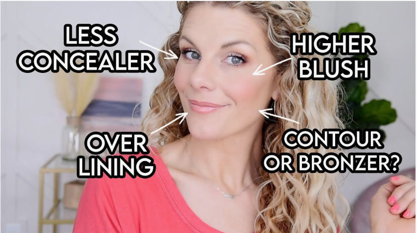 A woman with curly hair smiling with text callouts pointing to facial makeup placement including less concealer and higher blush, showcasing beauty tips for women over 40.