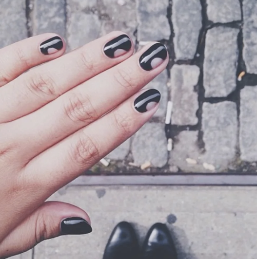 Short oval black manicure with half-moon negative space cutouts at the cuticle, creating stylish and modern office-friendly nail designs.