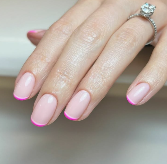 Short oval neutral-pink nails with thin, vibrant neon pink micro French tips, bringing a playful twist to office-friendly nail designs.