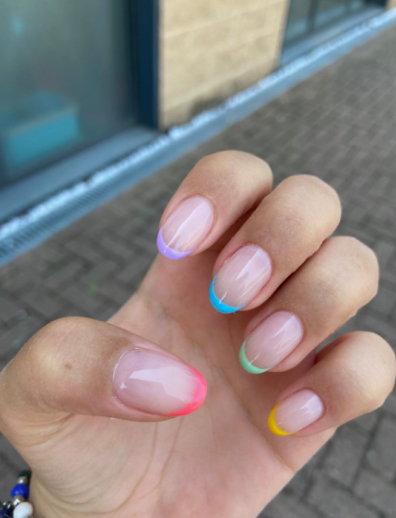 Short oval neutral-pink nails featuring vibrant multi-colored pastel French tips, offering a fun yet clean look for office-friendly nail designs.