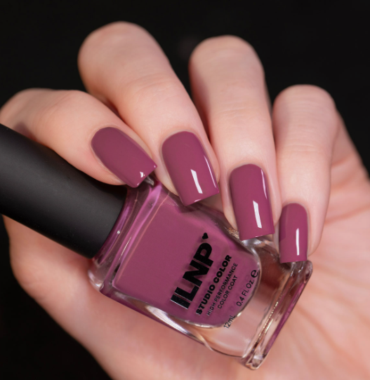 Short square-oval muted mauve-rose glossy ILNP polish nails holding a matching nail polish bottle, providing a professional and sophisticated look for office-friendly nail designs.