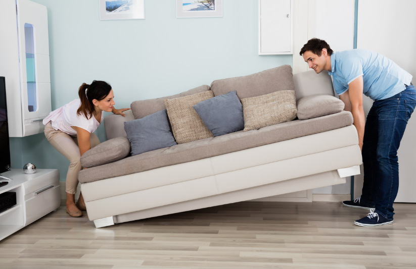 How to Make a Boring Room Look Better: 15 Simple Fixes Man and woman lifting and rearranging a beige sofa to redesign their living room layout and learn how to make a boring room look better.