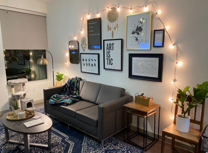 How to Make a Boring Room Look Better: 15 Simple Fixes Cozy living room featuring a dark grey sofa, a gallery wall illuminated by warm string lights, patterned blue rug, and a modern oval coffee table, demonstrating creative tips on how to make a boring room look better.