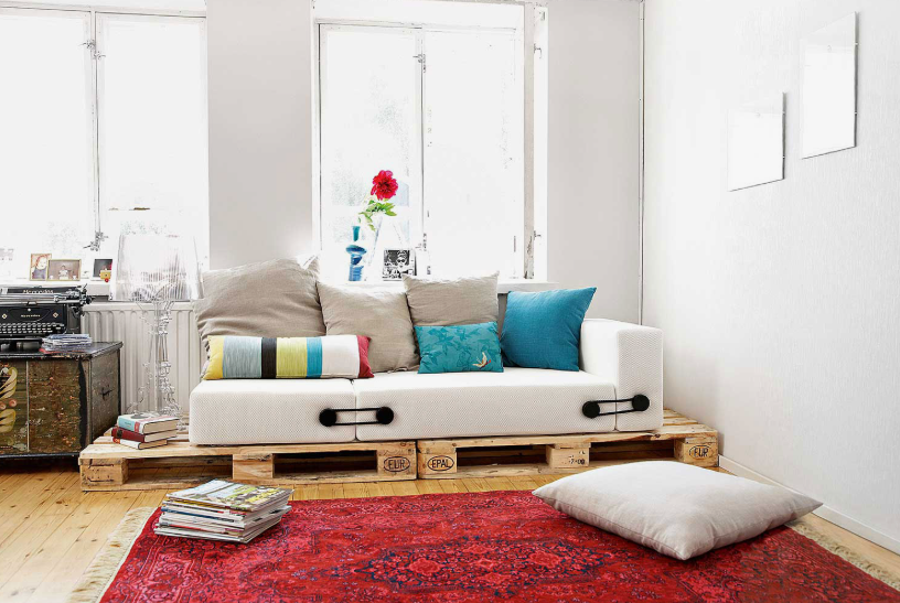 How to Make a Boring Room Look Better: 15 Simple Fixes Alt Text: Creative DIY living room featuring a custom pallet sofa styled with colorful pillows and a vibrant red rug, showcasing unique ideas on how to make a boring room look better.