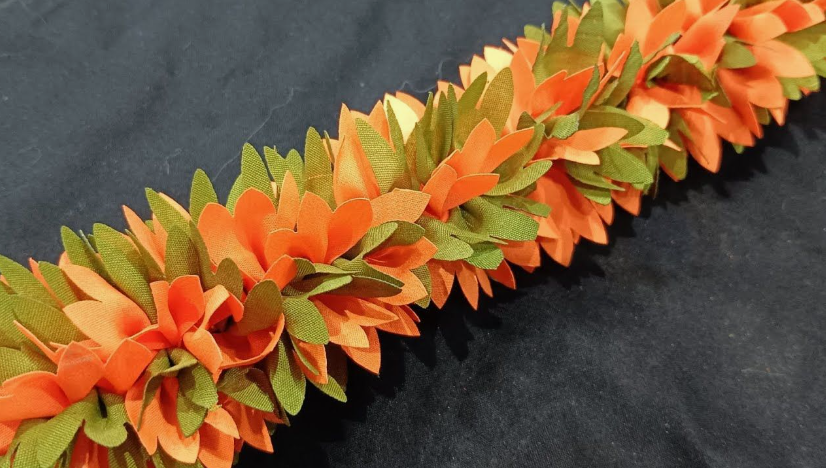 20 No-Sew DIY Crafts for Adults Close-up of a vibrant handmade orange and green fabric flower garland or lei against a dark background, showcasing creative no-sew DIY crafts for adults.