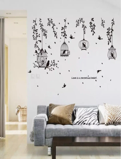 10 DIY Dorm Room Decor Ideas on a Budget That Look Amazing DIY dorm room decor ideas on a budget featuring a black wall sticker decal of hanging bird cages, branches, birds, and the inspirational quote "Love is a perpetual belief," displayed on a white wall above a grey sofa with patterned pillows.