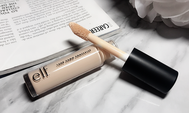 Tube of e.l.f. 16HR Camo Concealer with its large doe-foot applicator resting on a marble surface next to a book, highlighting best drugstore beauty products under $20.