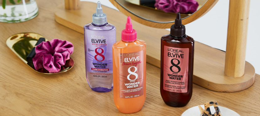Trio of L'Oréal Elvive Wonder Water lamellar rinse-out bottles in purple, orange, and brown arranged on a wooden vanity table, highlighting best drugstore beauty products under $20.