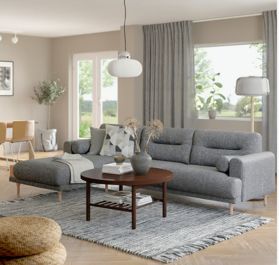 A modern, Scandinavian-inspired living room featuring a grey sectional sofa, a round wooden coffee table with a lower shelf, a textured grey rug, and a pendant light, presented as an interior styling project under the keyphrase one hour crafts.