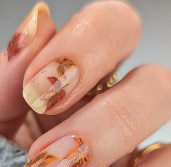 25 Short Fall Nail Ideas for 2026: Chic, Classy & Easy Designs Short fall nail ideas featuring translucent nude nails decorated with delicate painted autumn maple leaves and subtle gold glitter accents.