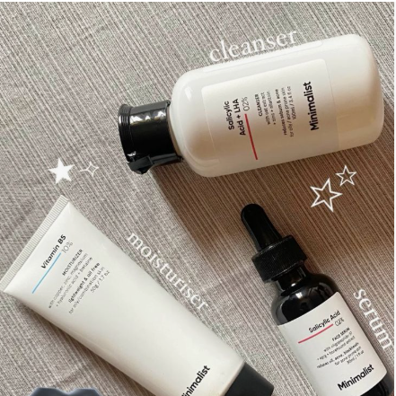 Beauty Products You Actually Need: A Minimalist Guide to Your Beauty Collection Flat lay arrangement of minimalist skincare products featuring a cleanser, Vitamin B5 moisturizer, and Salicylic Acid face serum on a textured neutral background.
