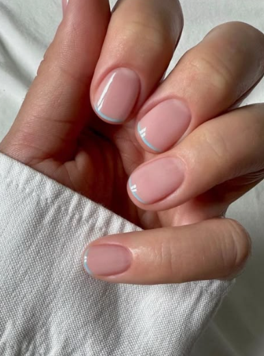A close-up of well-kept hands showcasing elegant short nails for women over 50, styled with a minimalist nude base and ultra-thin light blue micro French tips.