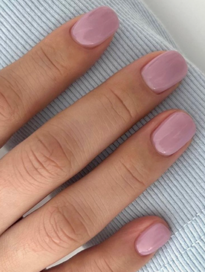 A close-up of a hand resting against a light blue textured sleeve, showcasing elegant short nails for women over 50 finished in a glossy, muted mauve pink polish.