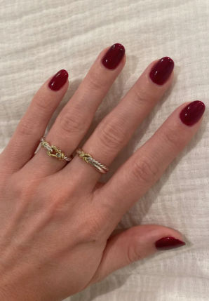 A close-up of a hand wearing two mixed-metal rings, showcasing elegant short nails for women over 50 polished in a rich, glossy deep burgundy red.