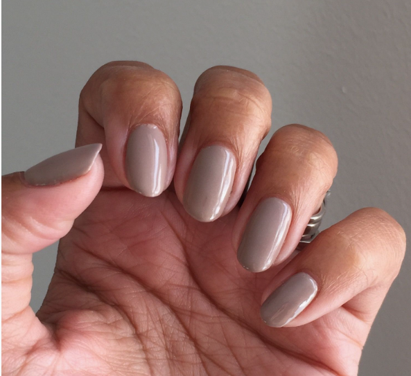 A close-up of a hand showcasing elegant short nails for women over 50 finished in a glossy, neutral taupe polish.