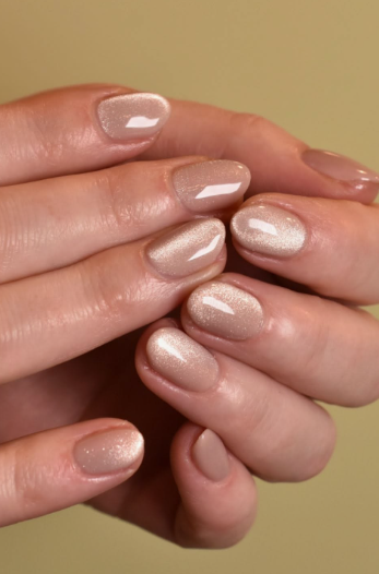 A close-up of hands with well-groomed, elegant short nails for women over 50, featuring a luminous beige cat-eye magnetic gel polish with a shimmering center beam.