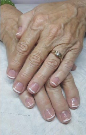 A close-up of hands wearing a gold diamond ring, showcasing elegant short nails for women over 50 styled with a classic French manicure featuring crisp white tips and a sheer nude base.