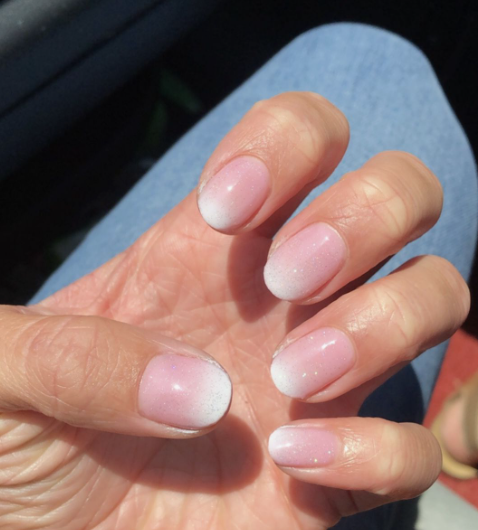 A close-up of a hand resting against blue denim, showcasing elegant short nails for women over 50 styled in a soft pink and white gradient baby boomer ombre with a subtle shimmer finish.