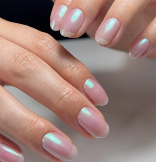 A close-up of well-groomed hands, showcasing elegant short nails for women over 50 styled in a glossy neutral base with an iridescent turquoise chrome glaze.