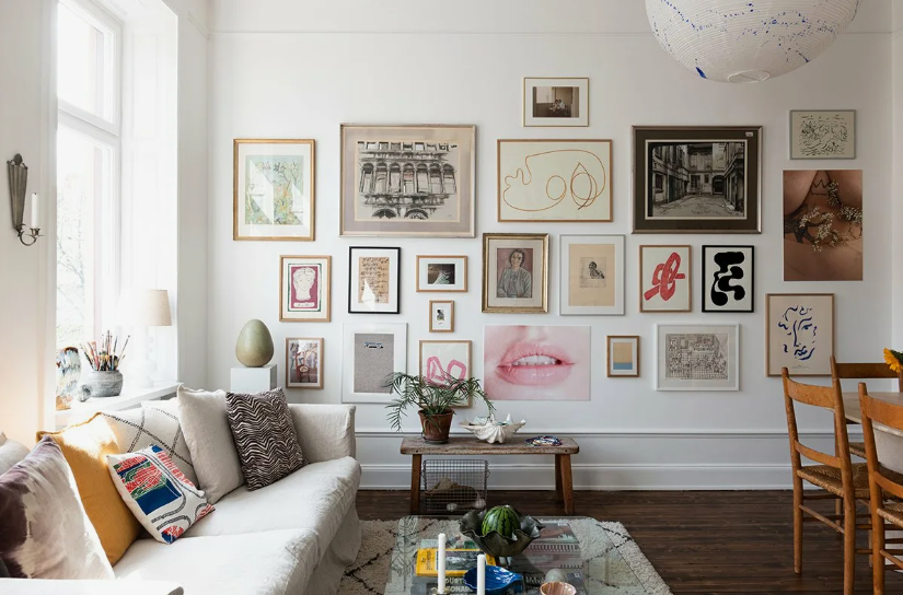 A bright, contemporary living room featuring an expansive gallery wall filled with diverse framed artwork and prints, a comfortable cream sofa styled with patterned throw pillows, and a wooden coffee table, capturing creative home decor ideas without buying anything.