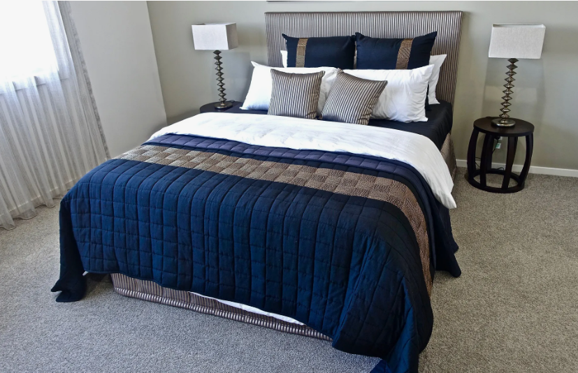 A neatly made bedroom with a textured navy blue duvet, matching accent pillows, and symmetrical bedside lamps, illustrating cozy home decor ideas without buying anything.