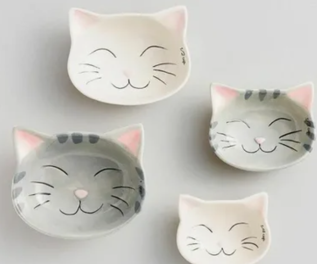 A charming collection of cat-shaped ceramic dishes and small bowls arranged on a neutral surface, showcasing delightful home decor ideas without buying anything by repurposing everyday tabletop items.