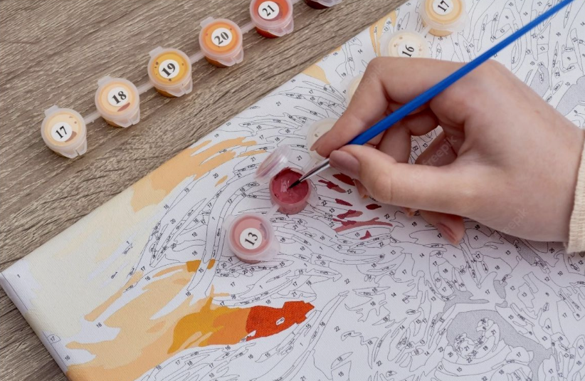 A close-up of a person painting on a numbered canvas using small pots of acrylic paint, perfect for crafts for people who arent artistic.