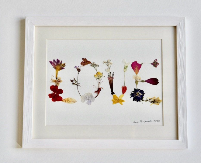 A framed pressed flower artwork spelling out the word "LOVE" using delicate dried petals and stems, demonstrating simple crafts for people who arent artistic.