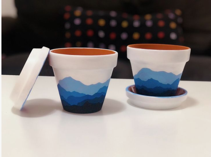 Two hand-painted terracotta plant pots and saucers featuring a layered blue mountain landscape design, making them ideal crafts for people who arent artistic.
