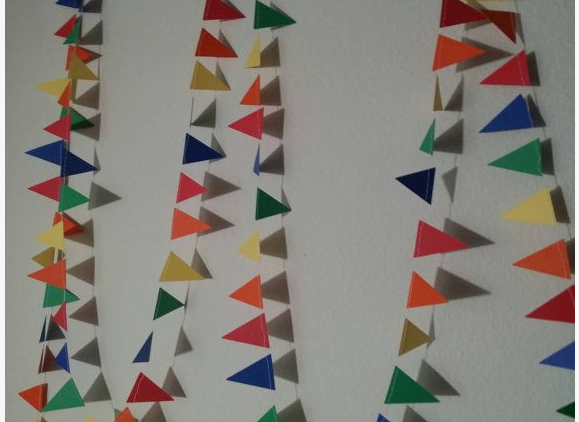 A string of colorful paper pennant flags hanging against a white wall, showcasing simple crafts for people who arent artistic.