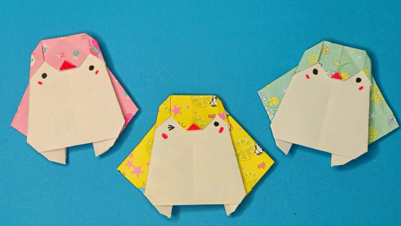 Three cute, folded origami penguin figures made from patterned craft paper against a blue background, showcasing fun crafts for people who arent artistic.