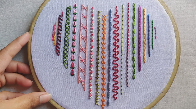 A wooden embroidery hoop holding white fabric stitched with colorful vertical lines of varied embroidery stitches forming a heart shape, illustrating crafts for people who arent artistic.