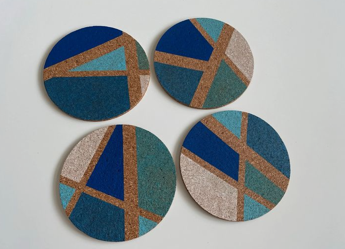 Four round cork coasters featuring geometric abstract painting in shades of blue, teal, and beige, showcasing creative home decor ideas without buying anything.