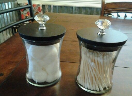 Two glass canisters with black lids and decorative diamond-shaped knobs, filled with cotton balls and cotton swabs, showcasing practical home decor ideas without buying anything.