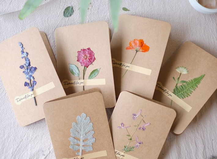A collection of handcrafted brown kraft paper notebooks and cards decorated with real pressed flowers and leaves, showcasing natural home decor ideas without buying anything.