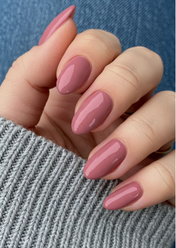 25 Nail Colors That Make Hands Look Younger A hand wearing a cozy gray sweater showcasing sleek almond-shaped mauve polish as one of the best nail colors that make hands look younger.